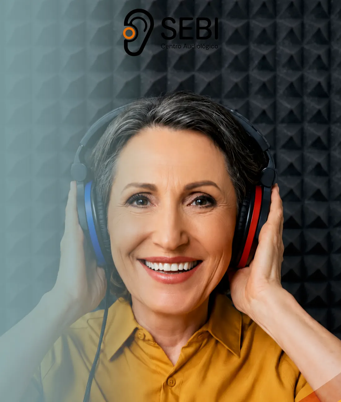 Paciente sonriente realizando una audiometría clínica con audífonos de diadema en una cabina audiológica de SEBI