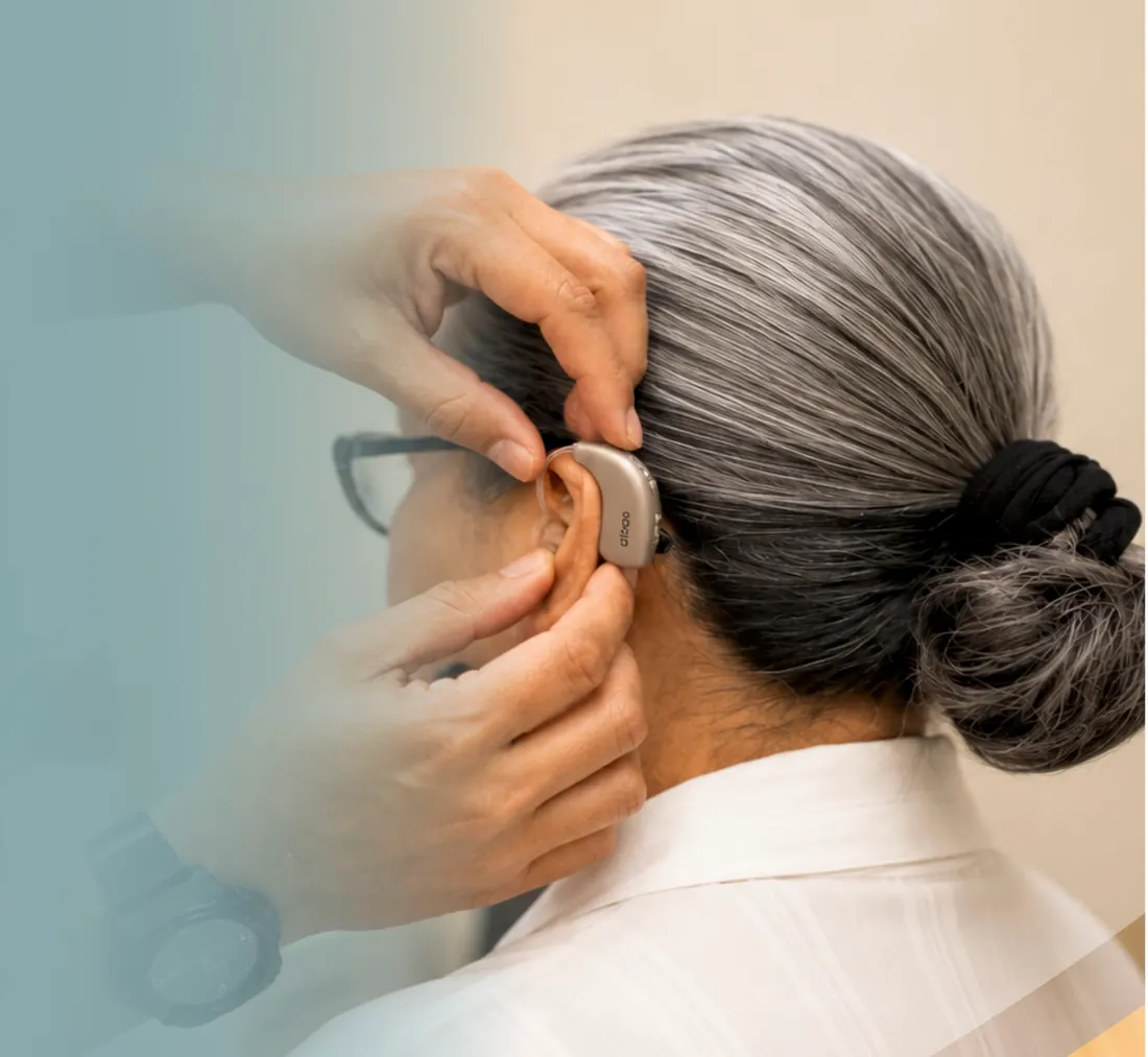 Profesional de SEBI colocando un audífono retroauricular detrás de la oreja de una paciente